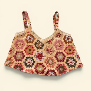 May include: A beige crop top with a floral patchwork design. The top features a V-neckline trimmed with lace and thin straps. The floral pattern includes red, green, and brown accents.