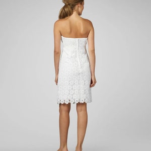 May include: A white strapless dress with a floral lace pattern. The dress has a fitted bodice and a slightly flared skirt.