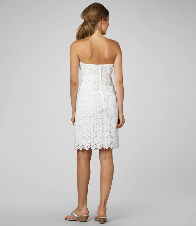 May include: A white strapless dress with a floral lace pattern. The dress has a fitted bodice and a slightly flared skirt.