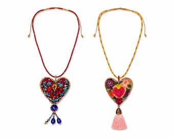 May include: Two heart-shaped pendant necklaces. One has a red beaded cord and a pendant with a cross design, blue beads, and a gold-colored accent. The other has a gold beaded cord and a floral pendant with a pink tassel.