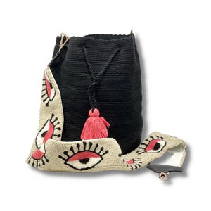 May include: Black crocheted bucket bag with a pink tassel and a beige eye-patterned strap.