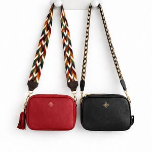 Puede incluir: Dos bolsos cruzados, uno rojo y otro negro, cuelgan sobre un fondo blanco. El bolso rojo tiene una correa estampada y una borla. El bolso negro tiene una correa de cadena dorada. Ambos bolsos tienen una cremallera dorada y un emblema dorado.
