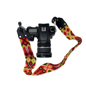 May include: A black Canon DSLR camera with a lens attached, hanging from a colorful woven strap with red, yellow, and pink accents.