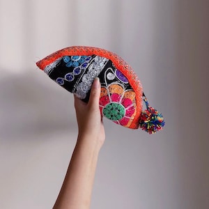 May include: A colorful embroidered pouch with a black background and a red trim. The pouch is decorated with floral patterns in shades of pink, green, blue, and orange. A small tassel hangs from the side.