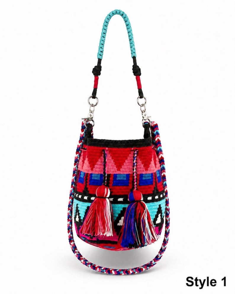 May include: A bucket bag featuring a vibrant woven pattern in red, black, blue, and turquoise. The bag includes a braided turquoise handle, a multi-colored braided shoulder strap, and two large tassels in red, blue, and white. Text reads Style 1.