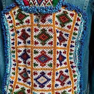 Pode incluir: Uma jaqueta de ganga com um design de contas coloridas nas costas. O design apresenta um padr&atilde;o geom&eacute;trico com quadrados e diamantes em tons de vermelho, azul, verde, branco e laranja.