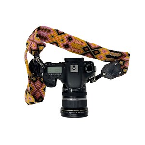 May include: A black DSLR camera with a pink and yellow patterned camera strap. The camera has a lens attached and is ready to take pictures.