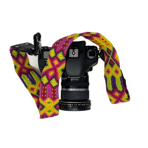 May include: A black DSLR camera with a colorful woven camera strap. The strap is pink, yellow, and green with a geometric pattern.