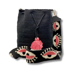May include: Black crocheted bucket bag with a pink tassel and a long adjustable strap with a white and pink eye design.