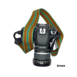 May include: A black DSLR camera with a colorful patterned strap. The strap features a zig-zag design in green, orange, and blue. The word "Green" is printed in the bottom right corner.