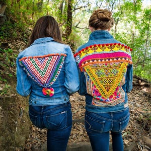 May include: Two denim jackets with colorful embroidered designs on the back. The jackets are decorated with geometric patterns and pom-poms.