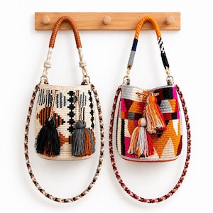 May include: Two woven bucket bags with drawstring closures and tassels. The left bag features a cream base with black and orange geometric patterns. The right bag displays a vibrant multicolored geometric design with orange, pink, and grey accents.