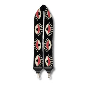 May include: Black adjustable shoulder strap with a repeating pattern of white and pink eyes. The strap has black leather ends with gold metal clasps.