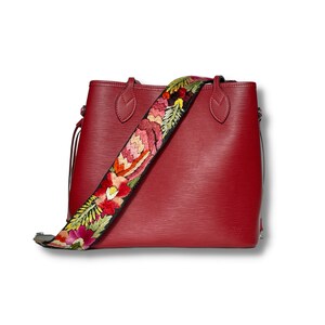 May include: A red leather tote bag with a floral embroidered strap. The bag has a top zipper closure and two handles.