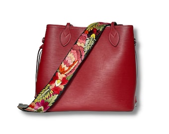 May include: A red leather tote bag with a floral embroidered strap. The bag has a top zipper closure and two handles.