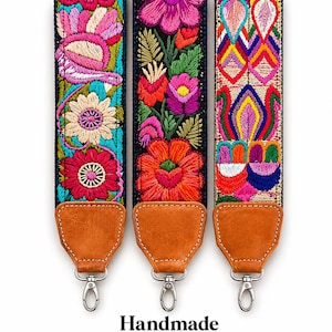 Puede incluir: Tres correas bordadas para bolsos con diseños florales coloridos. Cada correa presenta un patrón diferente de flores en tonos rosas, rojos, amarillos y azules sobre un fondo negro. Tienen extremos de cuero marrón y cierres plateados. La palabra "Handmade" está abajo.