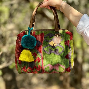 May include: A colorful, patterned handbag with a brown leather handle and two tassels. One tassel is teal and the other is yellow.