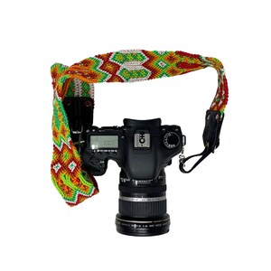 May include: A black DSLR camera with a lens attached, hanging from a colorful woven camera strap with red, green, white, and orange patterns.