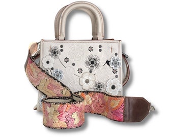 May include: White leather handbag with floral embroidery and a detachable strap. The strap is brown leather with pink and gold embroidery.