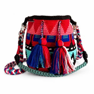 May include: A cylindrical crochet bucket bag featuring a vibrant geometric pattern in red, pink, blue, black, and white. The bag includes two large decorative tassels with matching colors and a thick, braided shoulder strap with silver hardware.