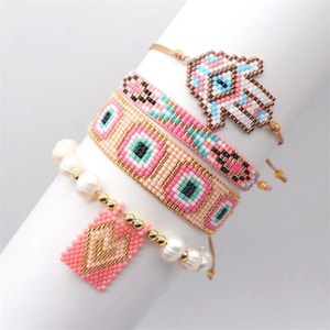 May include: Four beaded bracelets in shades of pink, white, and gold. One bracelet features a Hamsa hand design, while others have eye and geometric patterns. One bracelet includes pearls and a pink pendant.