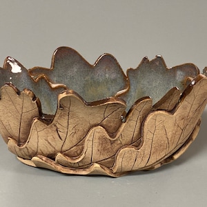 May include: A handcrafted ceramic bowl with a leaf design. The bowl's exterior is a warm brown, with detailed leaf impressions. The interior has a blue-green glaze. A unique decorative piece.