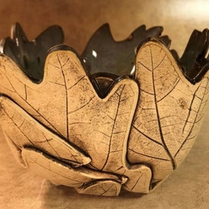 May include: A ceramic bowl with a leaf design. The bowl is beige with dark brown accents and a dark interior. The leaf pattern is detailed with visible veins. The bowl is approximately 6 inches in diameter and 4 inches tall.