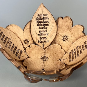 May include: A decorative ceramic bowl in a floral design. The bowl is shaped like a flower with petals and leaves. The text "And now abides Faith, Hope, Love, these three, but the greatest of these is Love" is inscribed on the leaves.