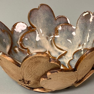 May include: A ceramic bowl with a floral design. The bowl is shaped like a flower, with petal-like edges in shades of brown and gray. The interior has a glossy finish. The bowl is approximately 6 inches in diameter.