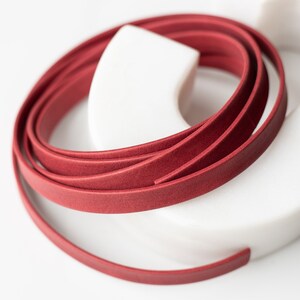 May include: A close-up of a red leather cord wrapped around a white object. The cord is smooth and has a slight sheen.
