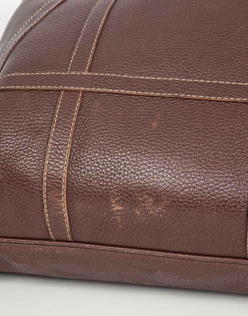 May include: A brown leather tote bag with a stitched design. The bag has a textured surface and appears to be well-worn.