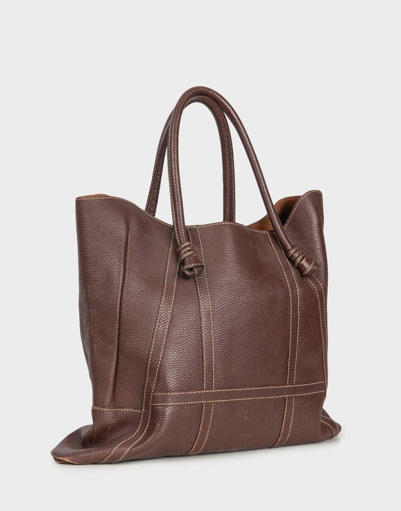 May include: A brown leather tote bag with knotted handles and stitched details.