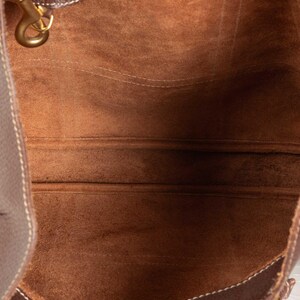 May include: The inside of a brown leather tote bag with a brown suede lining. The bag has a single strap and a small metal hook.