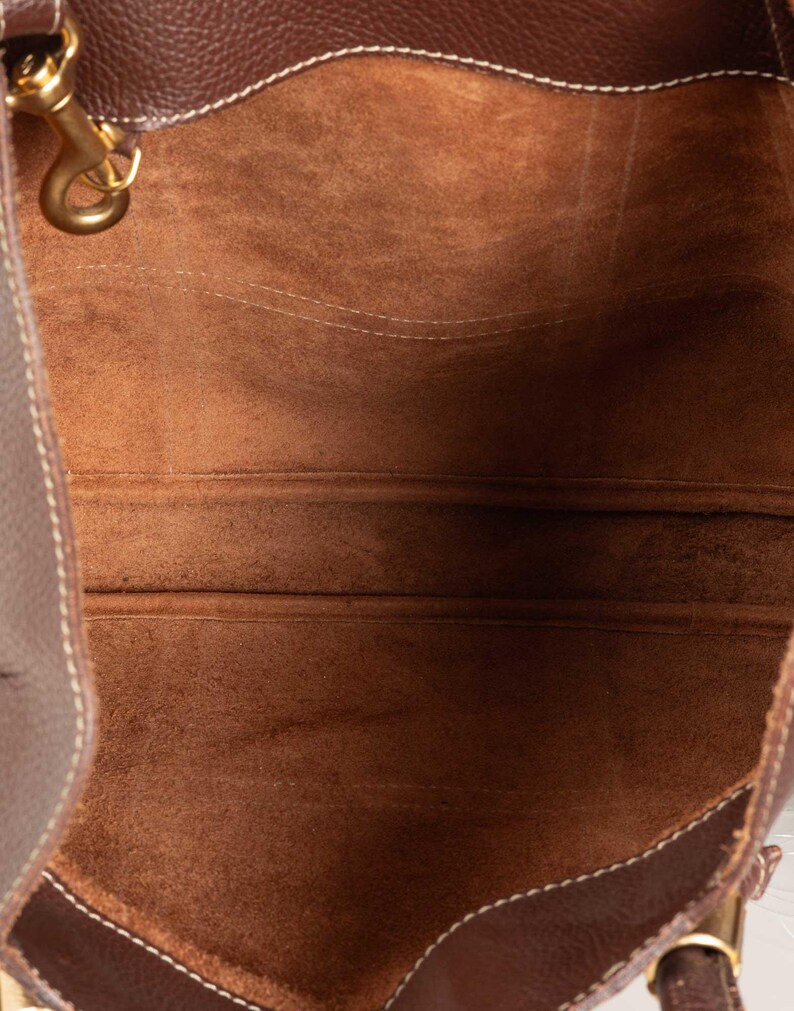 May include: The inside of a brown leather tote bag with a brown suede lining. The bag has a single strap and a small metal hook.