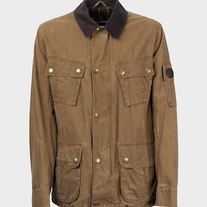 Può includere: Una giacca in cotone cerato marrone con colletto in velluto a coste e diverse tasche. La giacca ha un logo Barbour sulla manica sinistra.