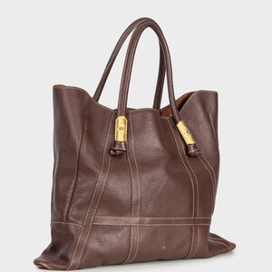 May include: A brown leather tote bag with gold hardware and a brown leather strap. The bag has a structured shape and a spacious interior.