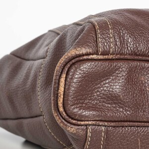 May include: A brown leather tote bag with a stitched design. The bag has a worn look and is made of a textured leather.