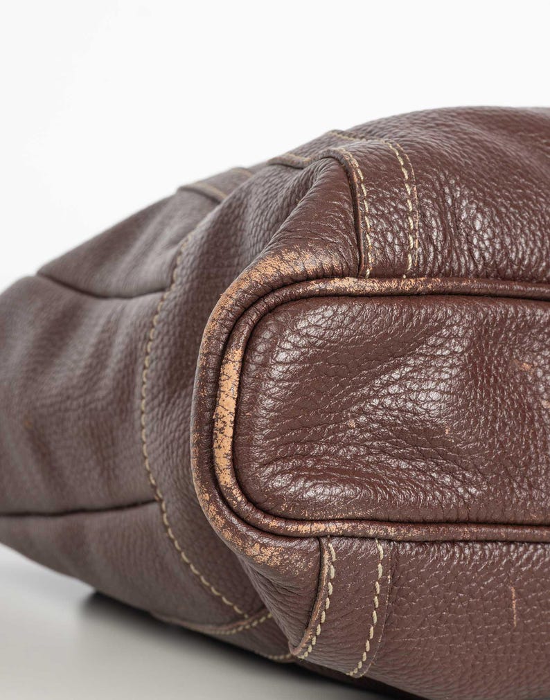May include: A brown leather tote bag with a stitched design. The bag has a worn look and is made of a textured leather.