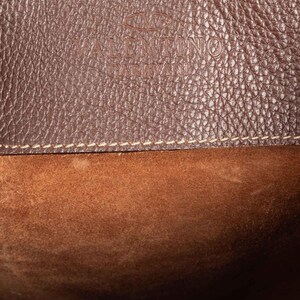 May include: Close-up of a brown leather bag with a stitched seam and the text "VALENTINO GARAVANI" embossed on the front.