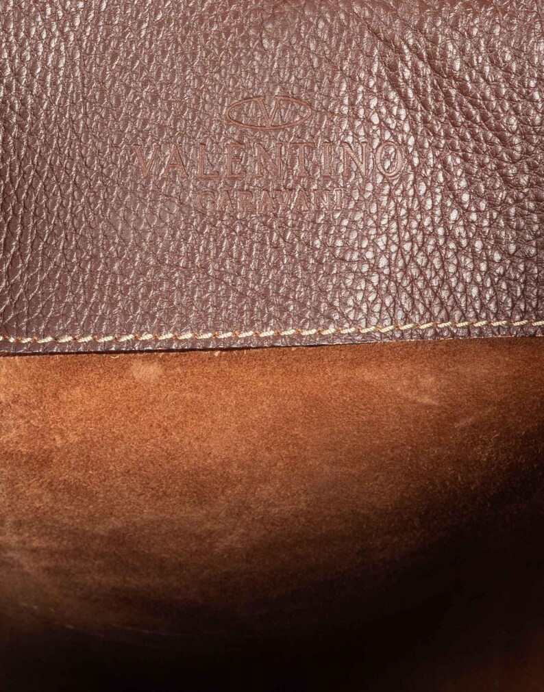 May include: Close-up of a brown leather bag with a stitched seam and the text "VALENTINO GARAVANI" embossed on the front.