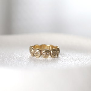 May include: A gold ring with a series of small skull designs, each with a diamond for eyes.