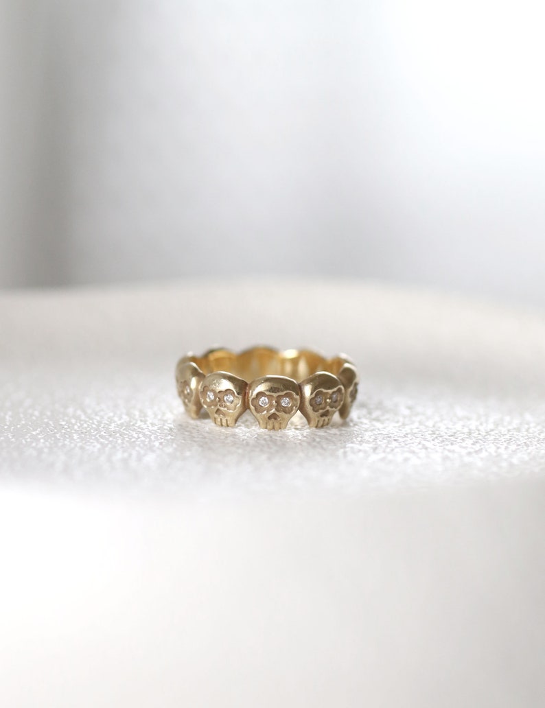 May include: A gold ring with a series of small skull designs, each with a diamond for eyes.