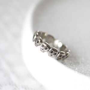 May include: A silver ring with a band of small skull designs, each skull has black diamond eyes.