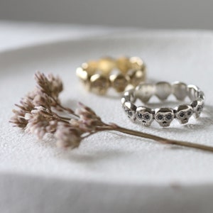 May include: Two silver skull rings with black stones on a white surface. The rings are stacked on top of each other.
