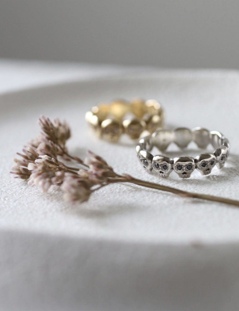 May include: Two silver skull rings with black stones on a white surface. The rings are stacked on top of each other.