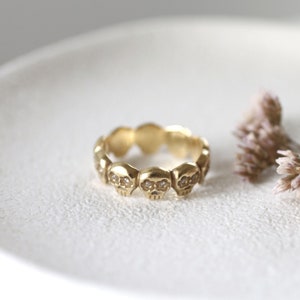 May include: A gold ring with a band of small skull designs, each with two small diamonds for eyes.