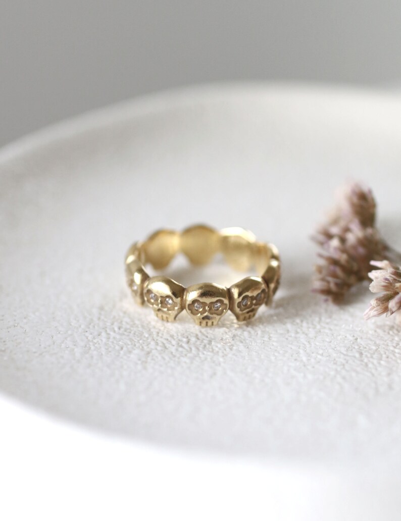 May include: A gold ring with a band of small skull designs, each with two small diamonds for eyes.