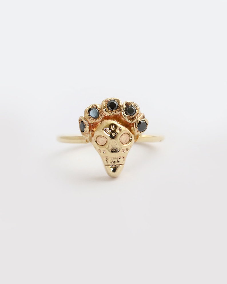 Puede incluir: Un anillo de oro con un dise&ntilde;o de calavera detallado y piedras preciosas negras alrededor de la cabeza de la calavera.