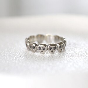 May include: A silver ring with a row of small skull charms, each with black diamond eyes.