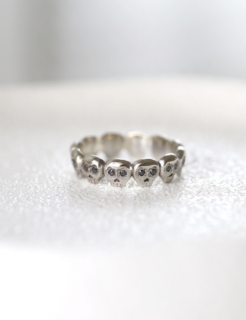 May include: A silver ring with a row of small skull charms, each with black diamond eyes.